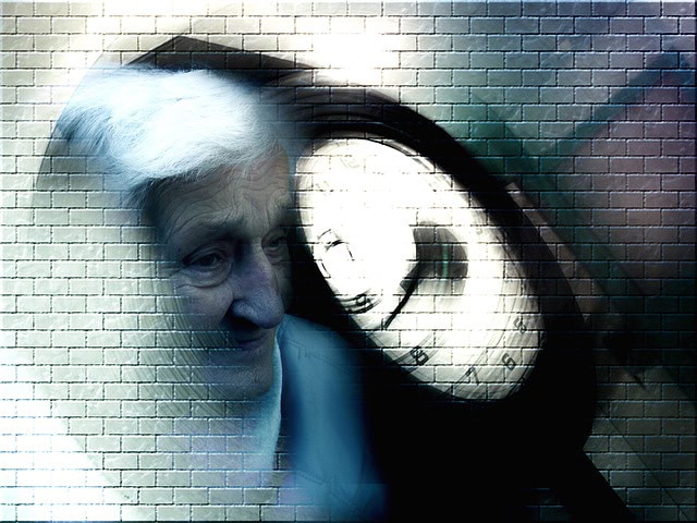 El rostro de una persona mayor se mezcla con un fondo que muestra un gran reloj antiguo contra una pared de ladrillos. La imagen tiene una cualidad surrealista y onírica con elementos borrosos, que transmiten sutilmente los primeros síntomas del Alzheimer.