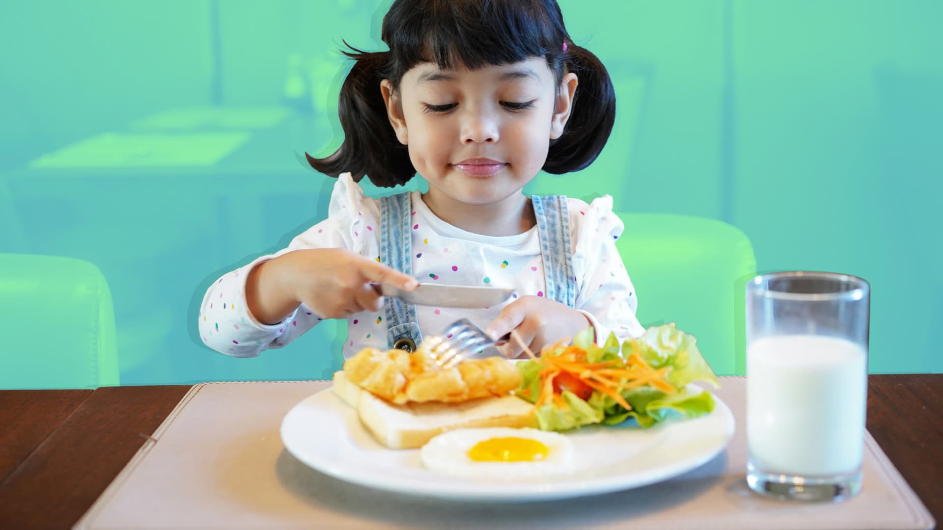 Una joven con coletas está sentada en una mesa disfrutando de una comida nutritiva que incluye tostadas, un huevo frito, ensalada y un vaso de leche. Ella está usando un tenedor y un cuchillo, mostrando signos tempranos de desarrollo tanto en sus habilidades motoras como en sus hábitos alimentarios.