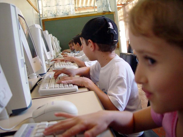 Niños sentados frente a ordenadores en un salón de clases, todos concentrados en escribir a máquina, participando en actividades de aprendizaje.