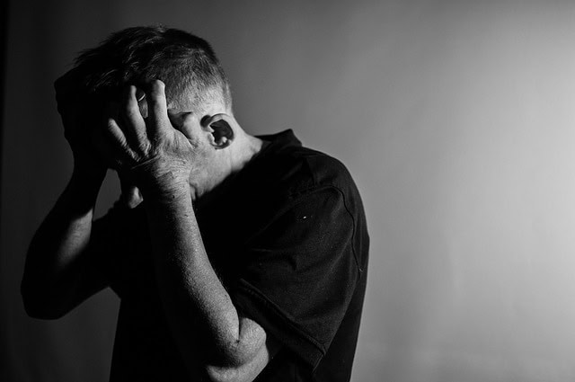 Un hombre de pie con las manos tapándose el rostro, vestido con una camisa oscura sobre un fondo liso, en una fotografía en blanco y negro, que evoca la lucha silenciosa contra el TDA/H en adultos.