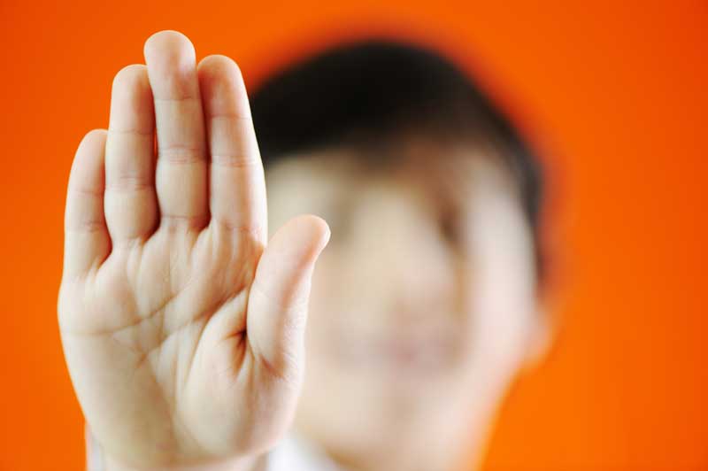 Una persona levantando la mano con los dedos extendidos en un gesto de parada sobre un fondo naranja, lo que refleja el estrés de la vida diaria. La cara está borrosa y no enfocada.