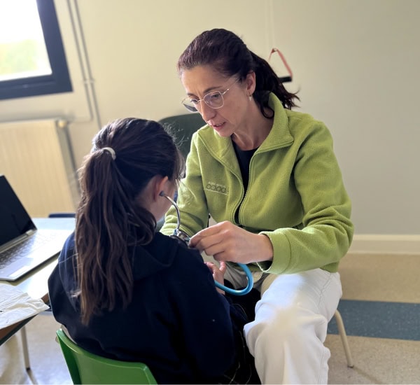 Un profesional sanitario con una chaqueta verde utiliza un estetoscopio para examinar a una persona sentada con el pelo largo en un entorno clínico, ofreciendo conocimientos alineados con Psicología en Sevilla.