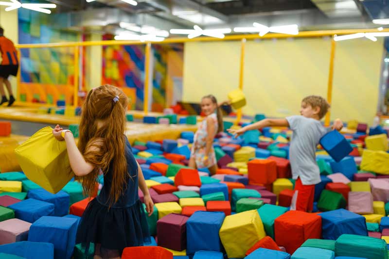 Los niños juegan en un patio interior lleno de coloridos bloques de espuma, lo que favorece el juego imaginativo y la diversión.