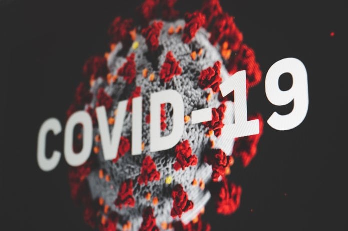 Primer plano de un modelo 3D creado digitalmente del virus COVID-19 con el texto "COVID-19" superpuesto en letras blancas, que simboliza cómo debemos enfrentar este desafío mientras navegamos en la era COVID.