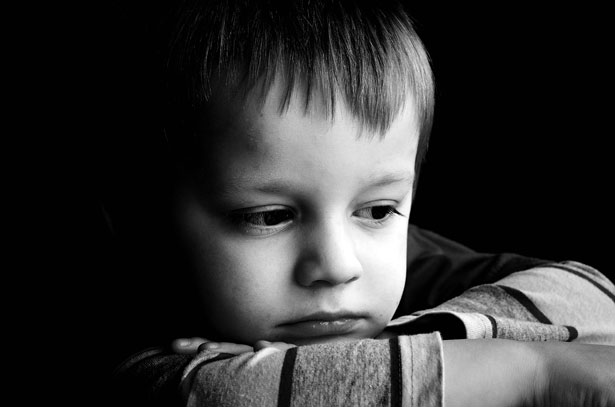 Fotografía en blanco y negro de un niño de aspecto triste, con la barbilla apoyada en los brazos cruzados y una expresión pensativa en el rostro, tal vez reflexionando sobre la reciente separación o ruptura de pareja de sus padres.